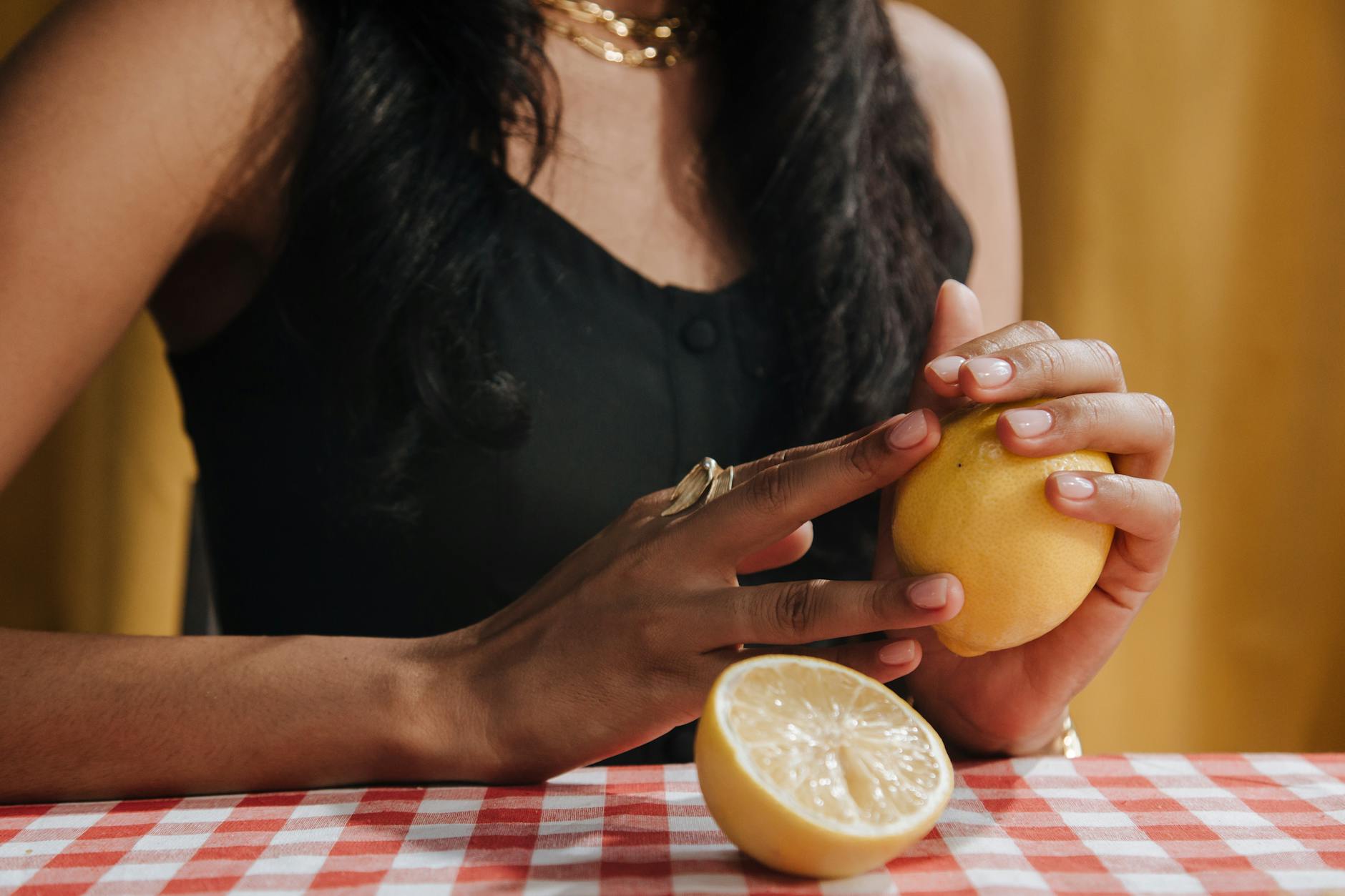 Close-up of hands holding a fresh lemon at a dining table, symbolizing natural pleasure and wellness