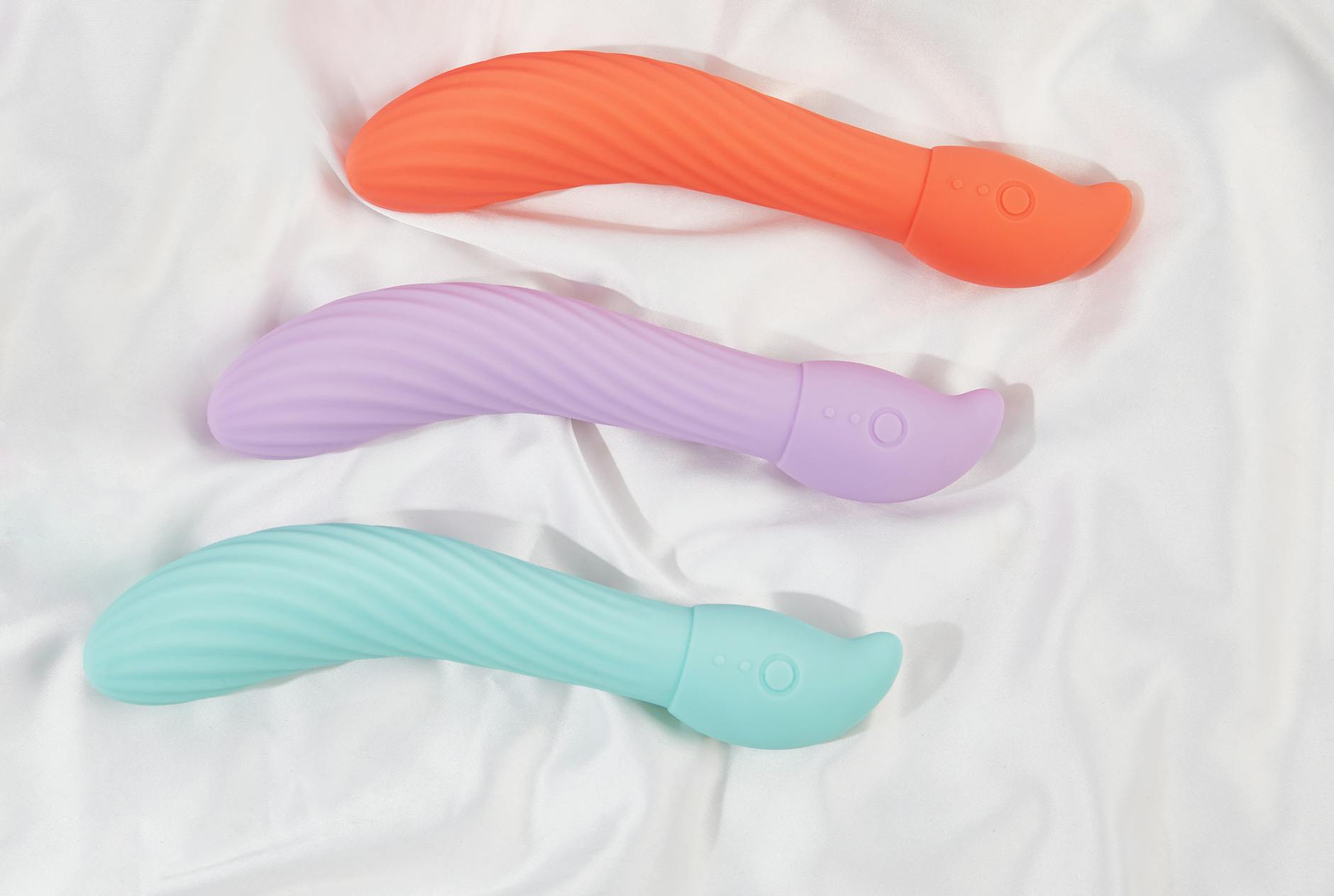 Three colorful vibrators arranged on white fabric, highlighting their smooth texture and design.