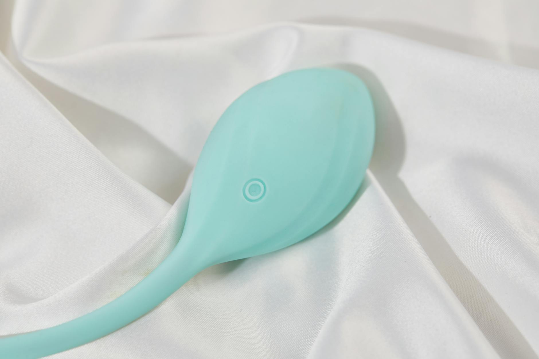 A stylish teal clitoral vibrator on smooth silk fabric