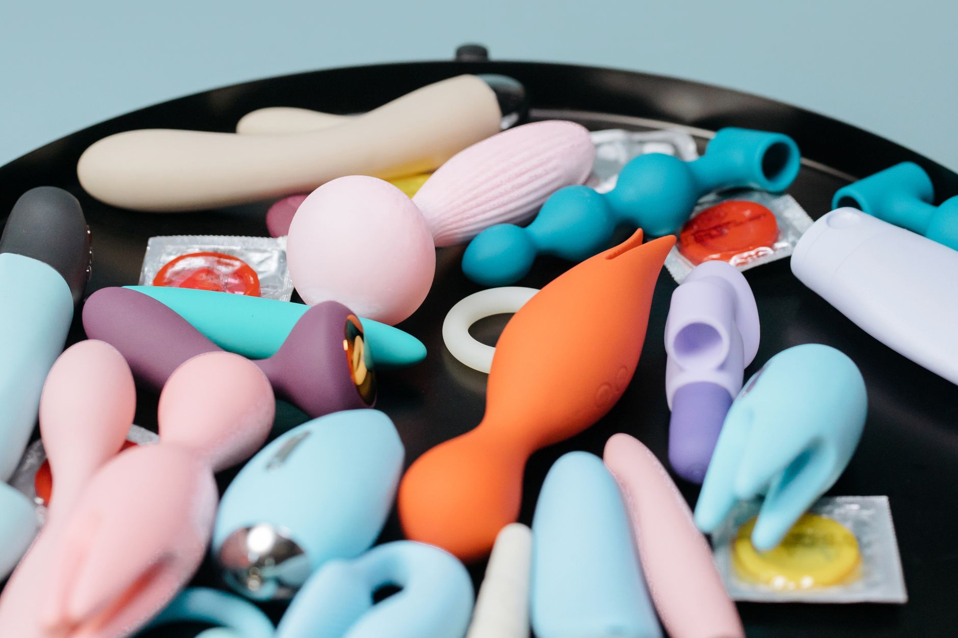 A collection of various clitoral vibrators and toys displayed on a black tray, showing different shapes and colors.