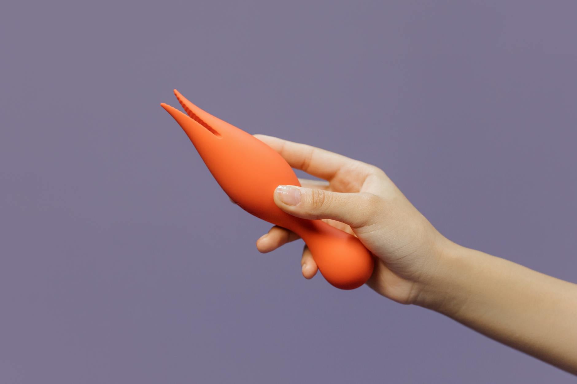 Hand holding an orange vibrator against a minimalistic purple backdrop, showcasing modern sensuality and simplicity.