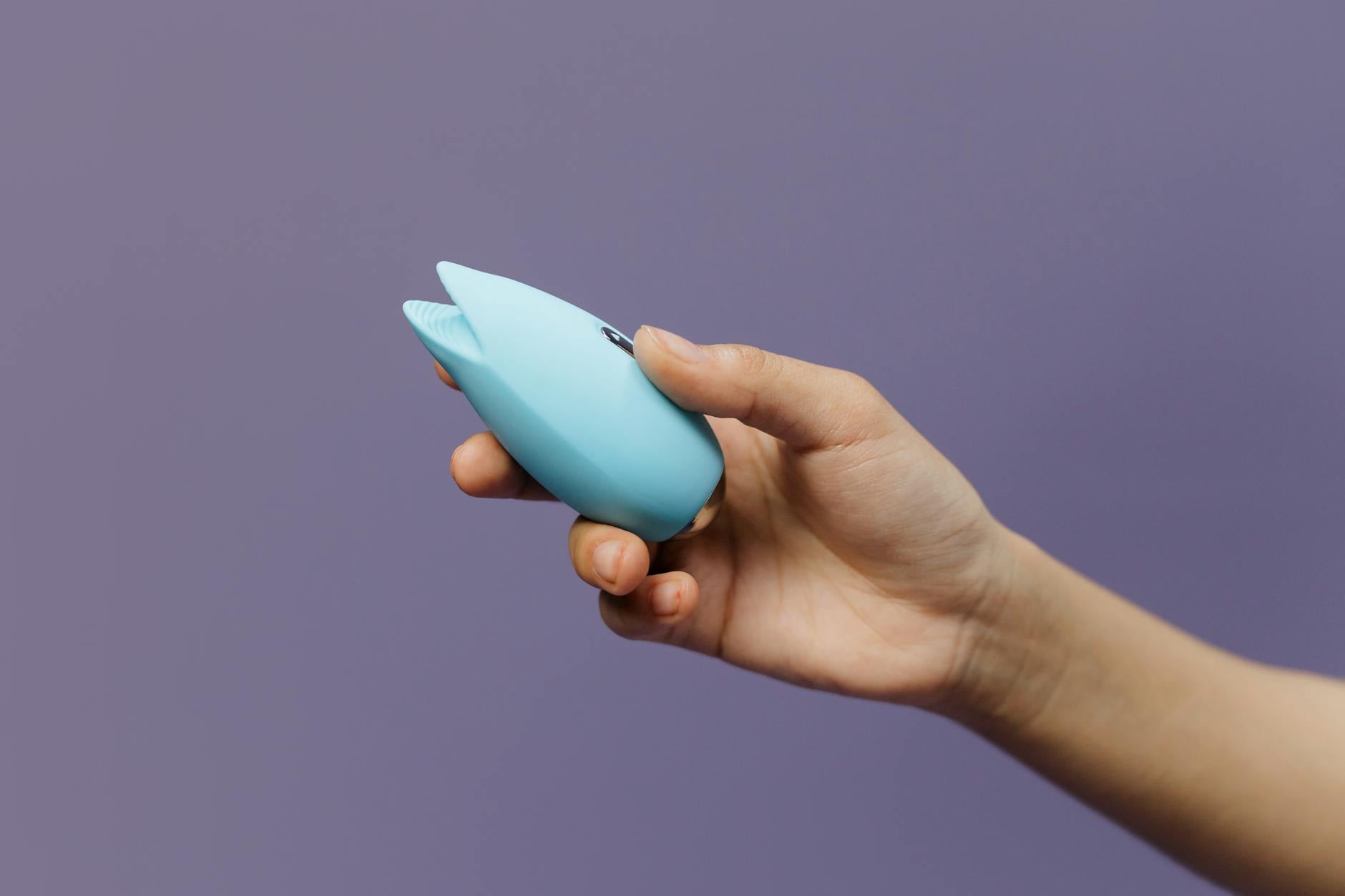 A blue lemon-shaped vibrator held in hand against a purple background