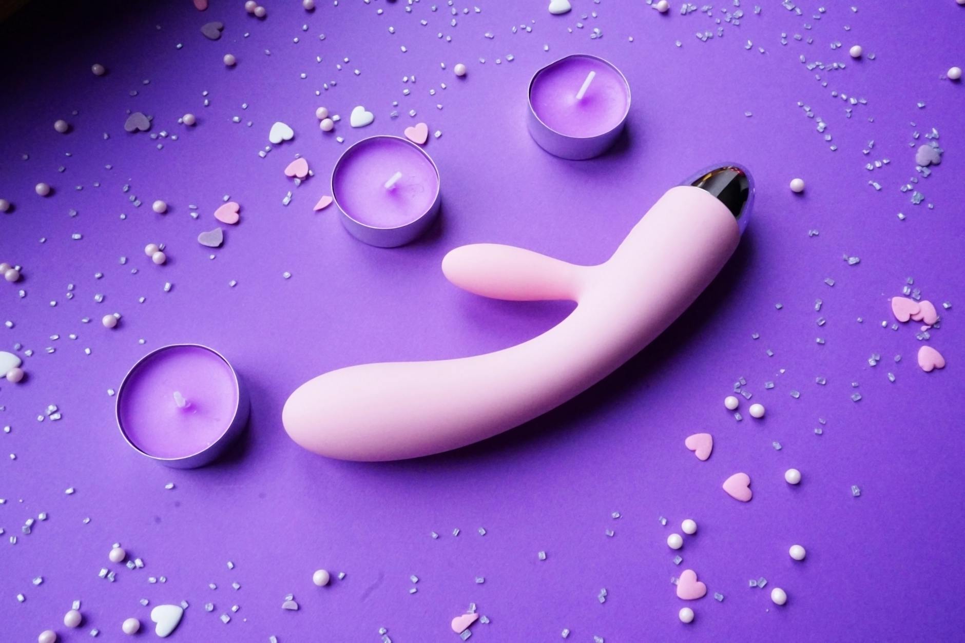 Pink clitoral vibrator on purple background with hearts and candles